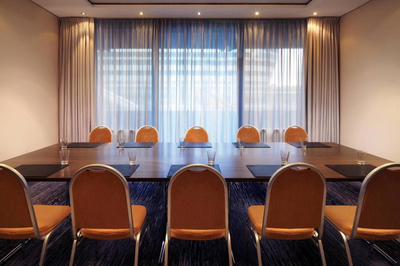 Frankfurt Airport Marriott Hotel Φραγκφούρτη Εξωτερικό φωτογραφία The photo depicts a meeting room featuring a long rectangular table surrounded by several chairs. The chairs are orange with a simple design. On the table, there are water glasses placed in front of each chair, indicating it's ready for a meeting or 