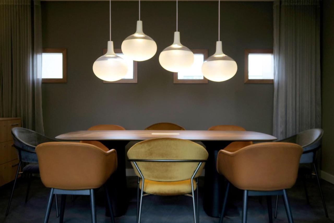 Frankfurt Airport Marriott Hotel Φραγκφούρτη Εξωτερικό φωτογραφία The photo shows a modern dining area featuring a long table surrounded by several chairs. Above the table, there are four pendant lights with a sleek design that emit a warm glow. The walls are painted in a muted tone, and there are two small windows
