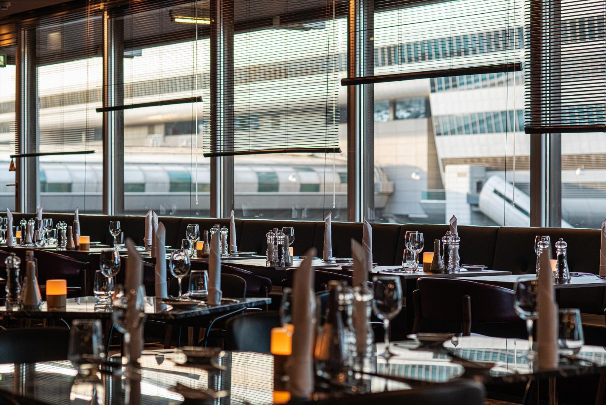 Frankfurt Airport Marriott Hotel Φραγκφούρτη Εξωτερικό φωτογραφία The photo shows the interior of a restaurant with a modern design. The tables are elegantly set with glassware, folded napkins, and small candles, creating a sophisticated dining atmosphere. Large windows allow natural light to flood the space and pr