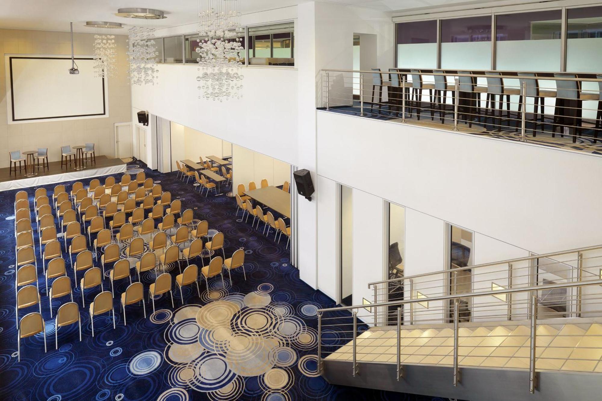 Frankfurt Airport Marriott Hotel Φραγκφούρτη Εξωτερικό φωτογραφία The photo shows a spacious, modern conference or event room. There are rows of tan chairs set up for an audience, indicating that it is likely prepared for a presentation or meeting. The flooring features a circular patterned carpet, adding a decorat