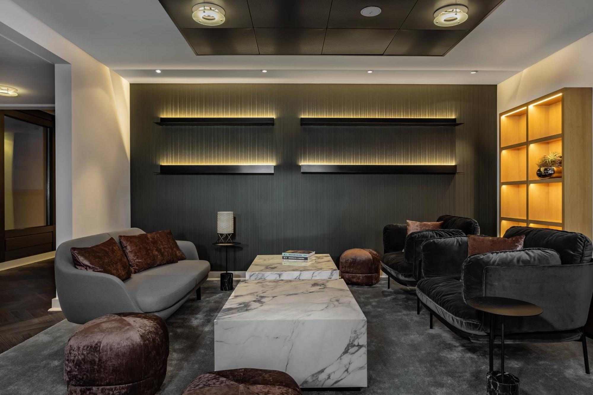 Frankfurt Airport Marriott Hotel Φραγκφούρτη Εξωτερικό φωτογραφία The photo shows a modern interior space, likely a lounge or waiting area. The decor includes a marble coffee table positioned in the center, surrounded by several stylish armchairs and a sofa, featuring dark and earthy tones. Ambient lighting is stra